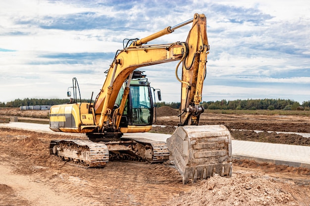 Foto una pesada excavadora de orugas con un gran cucharón se está preparando para trabajar frente a una casa de paneles en construcción. equipo pesado de construcción para movimiento de tierras. excavadora de cantera.