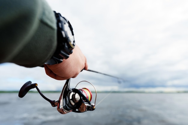 Pesca Closeup de fiação nas mãos de um pescador contra o fundo do lago Foco seletivo na mão