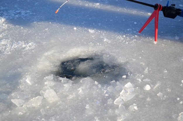 Pesca en hielo de invierno Pesca en hielo invierno La caña de pescar se encuentra cerca del agujero en el río de hielo