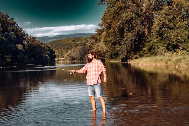 Pesca joven barbudo. Hombre pesca con mosca. Tiempo de fin de semana. Pescador feliz. En el río o en el lago. Habilidades de pesca. Relajarse mientras disfruta de la afición.