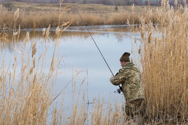 Pesca en los juncos para girar en aguas tranquilas Un hombre con ropa de camuflaje en clima fresco está pescando en la orilla del río