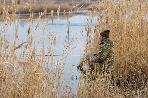 Pesca en los juncos para girar en aguas tranquilas Un hombre con ropa de camuflaje en clima fresco está pescando en la orilla del río