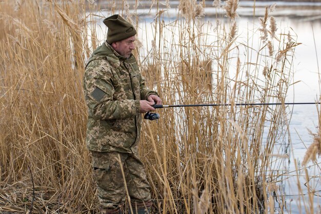 Pesca nos juncos para girar em águas tranquilas Um homem com roupas de camuflagem em clima frio