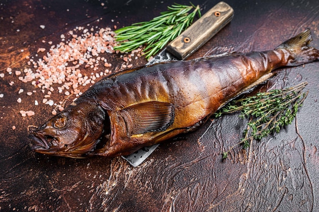 Foto pescado ahumado caliente lucioperca o lucioperca sobre una tabla de madera con hierbas. fondo oscuro. vista superior.