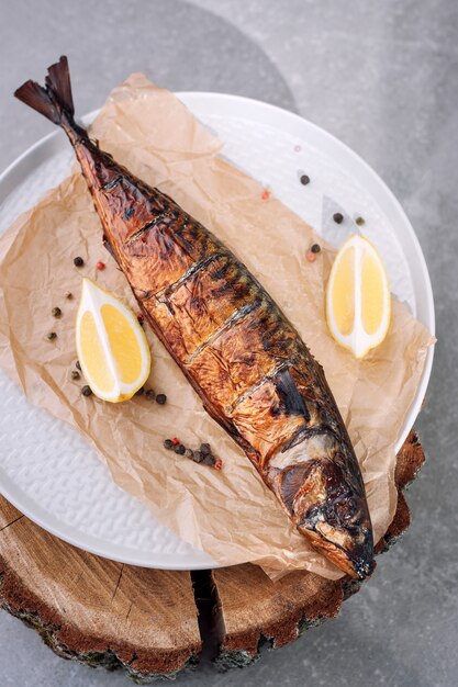 Pescado ahumado con rodajas de limón y pimienta sobre papel de respaldo sobre fondo de madera de fumar, vista superior.