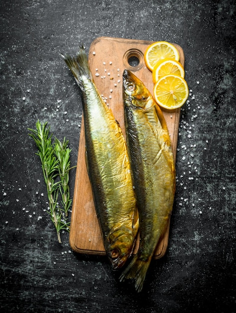 Pescado ahumado en una tabla de cortar con limón y romero