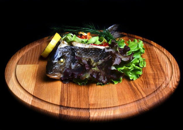 Pescado al horno con verduras sobre una plancha de madera.