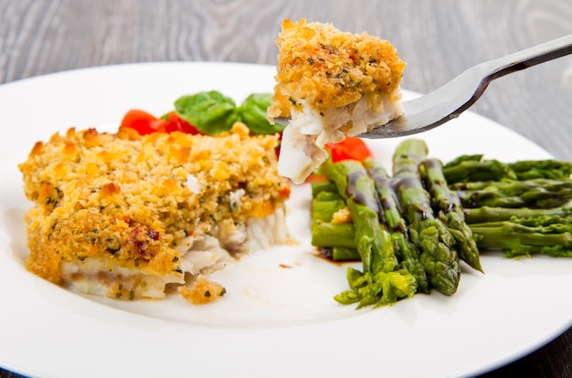 Pescado de bacalao con pan rallado y espárragos.