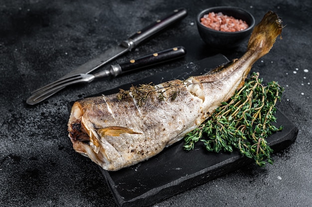 Pescado blanco de bacalao asado al tomillo sobre tabla de mármol. Fondo negro. Vista superior.