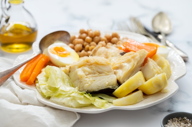 Pescado cocido con verduras y huevo cocido en un plato blanco