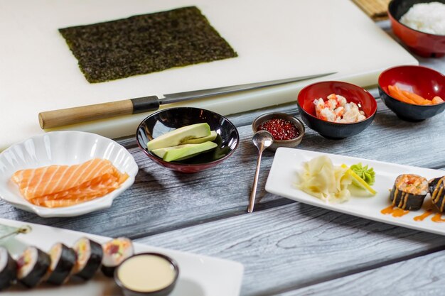 Pescado crudo y aguacate en rodajas. Cuenco pequeño con caviar rojo. Ingredientes de sushi en mesa de madera. Mesa del chef en restaurante japonés.