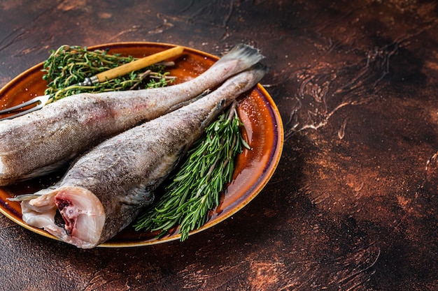 Foto pescado crudo de bacalao o bacalao en plato rústico con hierbas y tenedor. fondo oscuro. vista superior. copie el espacio.