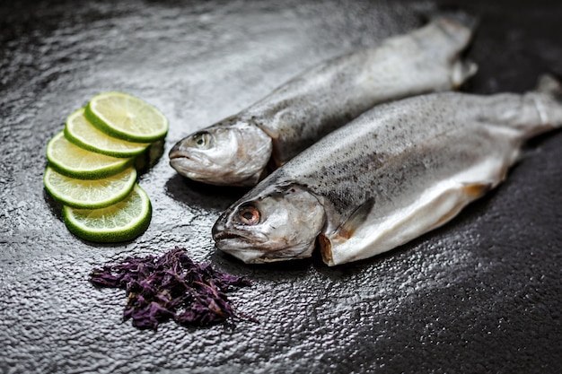 Pescado crudo e ingredientes para cocinar. Truchas de río, lima y hierbas en texturas oscuras.