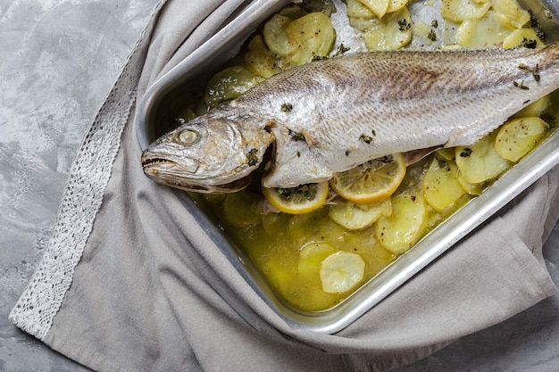 Pescado crudo fresco de lubina preparado para asar con papas