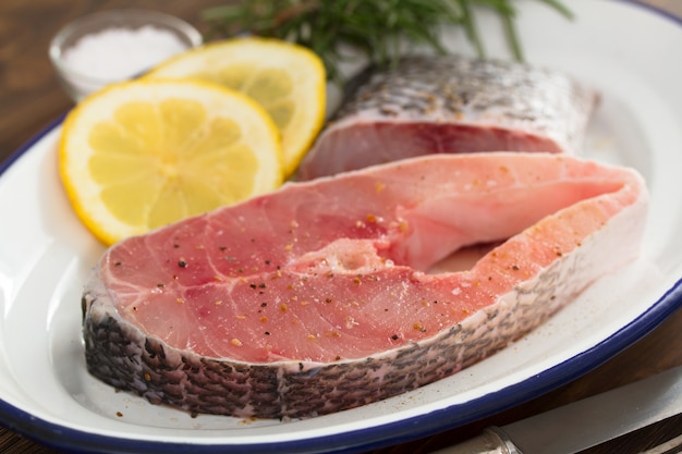 Pescado crudo con limón en plato sobre superficie marrón