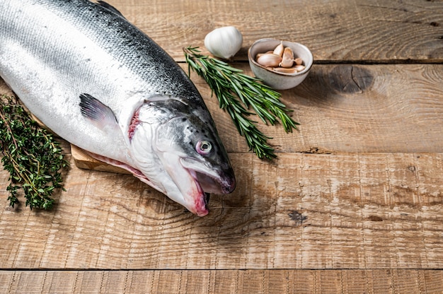 Pescado crudo de salmón marino en una mesa de cocina de madera con hierbas. Fondo de madera. Vista superior. Copie el espacio.