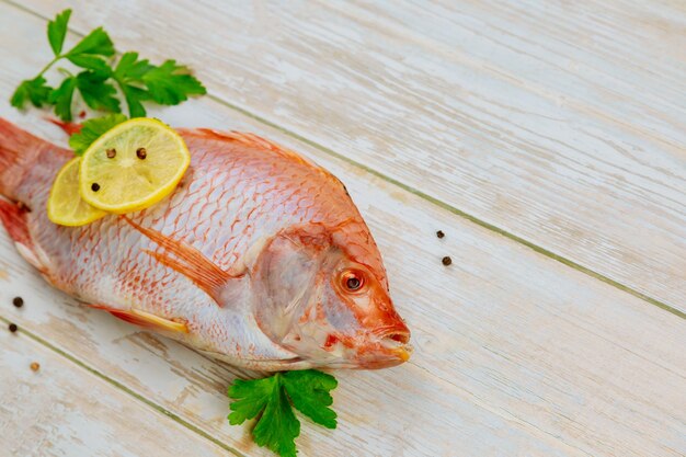 Pescado crudo de tilapia roja con hierbas y limón en madera