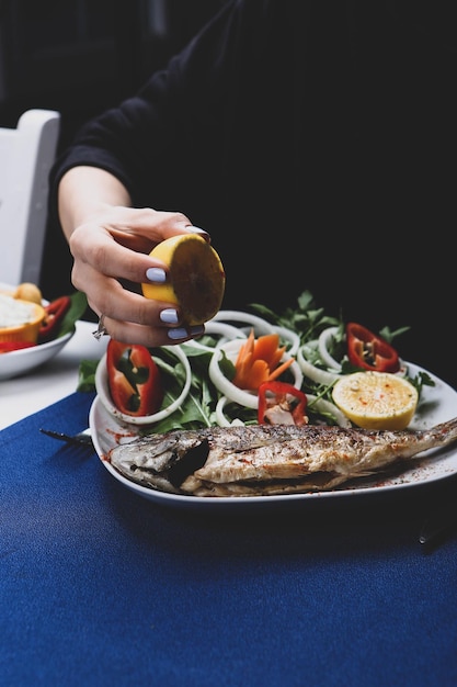 Pescado cupra de besugo frito en un plato blanco con rúcula de jardín de cebolla y rodajas de limón