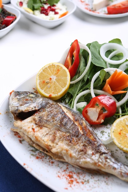 Pescado cupra de besugo frito en un plato blanco con rúcula de jardín de cebolla y rodajas de limón