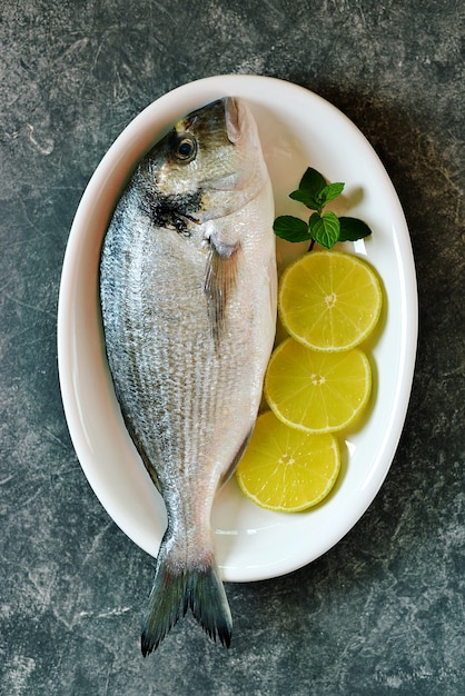 Pescado dorado crudo fresco con rodajas de limón y hojas de menta