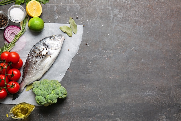 Pescado dorado crudo con ingredientes en hormigón gris, vista superior