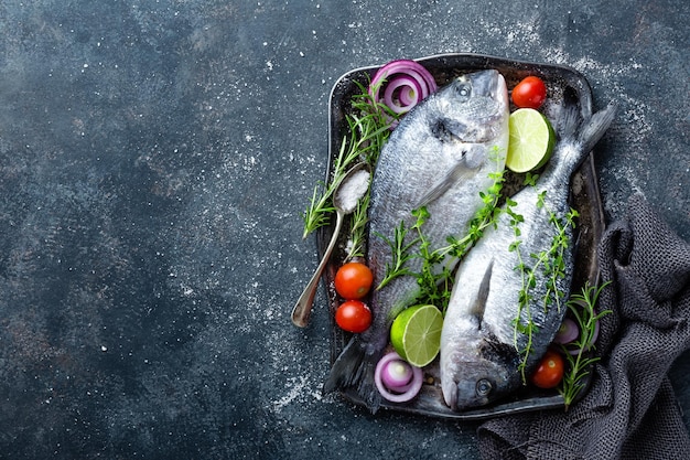 Foto pescado dorado fresco y sin cocinar o brasa de mar con ingredientes para cocinar en fondo oscuro vista de arriba