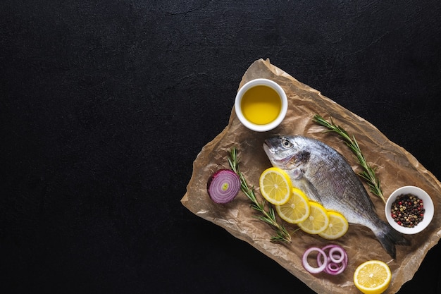 Pescado Dorado fresco crudo sobre papel de cocina preparado para cocinar con especias sobre un fondo negro. Mariscos. Vista superior. Copie el espacio.