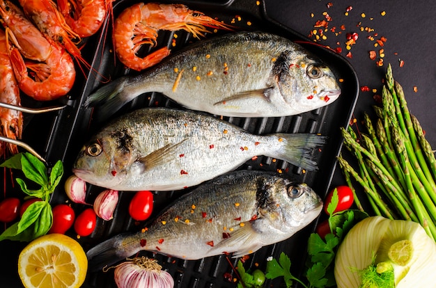 Pescado dorado fresco y langostinos tigre en una sartén de hierro y verduras para cocinar