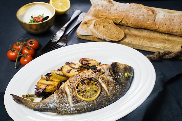 Pescado dorado a la parrilla en un plato blanco, adornar papas fritas.