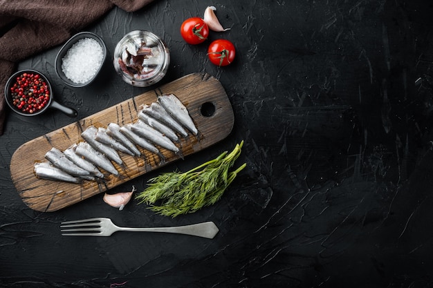 Pescado enlatado de anchoas en una lata de marisco, sobre tabla de cortar de madera, sobre negro