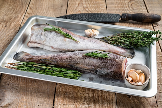 Pescado entero de bacalao crudo en bandeja de acero con tomillo y romero