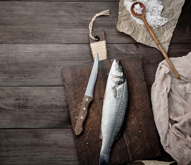 Pescado entero fresco de la lubina en la tabla de cortar marrón