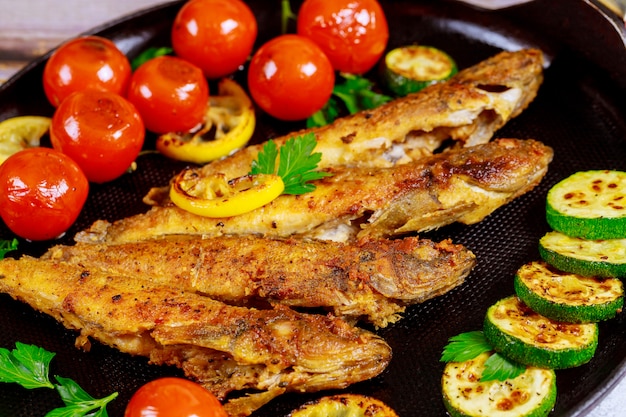 Pescado entero frito con vegetales en una sartén negra. De cerca.