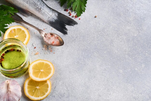 Pescado fresco Lubina cruda con sal, pimienta, perejil, aceite de oliva y limón en la tabla de cortar sobre fondo rústico de hormigón gris claro Fondo de cocina de alimentos Vista superior espacio de copia