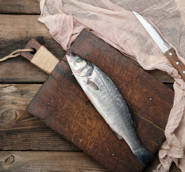 Pescado fresco de lubina entera en tabla de cortar marrón