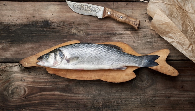 Pescado fresco de lubina entera en tabla de cortar marrón