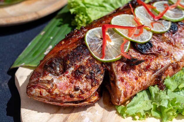 Pescado frito con ensalada verde fresca y limón de Bali Indonesia cerrar Delicioso pescado de mar asado con limón en un plato de madera en el restaurante