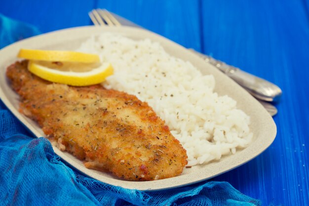 Foto pescado frito con limón y arroz hervido en un plato