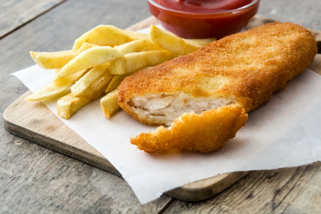 Pescado frito con patatas fritas británicos tradicionales en la tabla de madera.