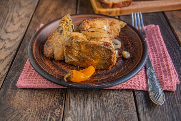 Foto pescado frito en un plato de cerámica con condimentos y pan en una mesa de comedor de madera