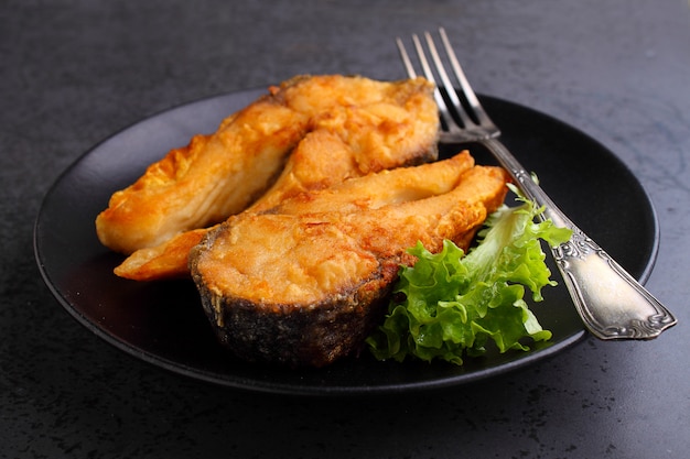 Pescado frito en un plato negro con lechuga