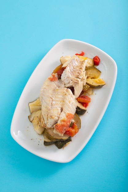 Pescado frito con verduras al horno en plato blanco