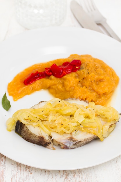 Pescado hervido con cebolla y puré de calabaza en un plato blanco