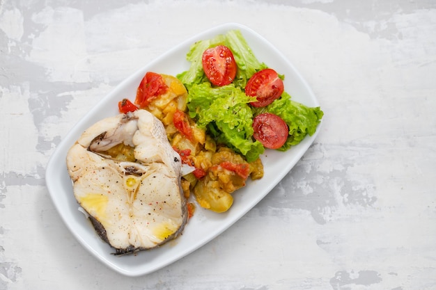 Pescado hervido con ensalada en un plato blanco