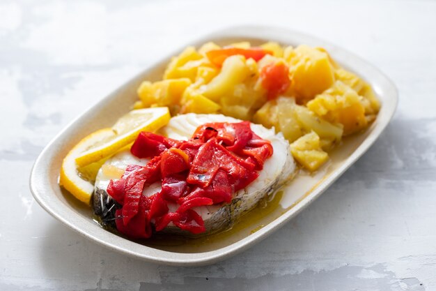 Pescado hervido con pimiento rojo, verduras y aceite de oliva en un plato blanco