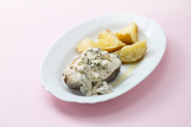 Pescado hervido con salsa tártara y patata hervida en un plato blanco