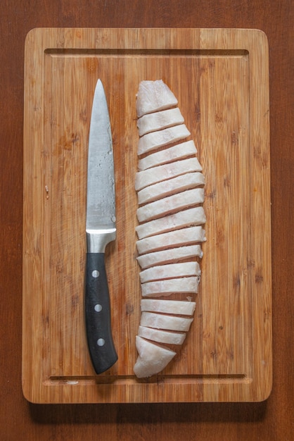 Foto pescado medio congelado en una tabla de madera cortado en rebanadas finas por un gran cuchillo detalles de primer plano concepto de cocina casera y comida saludable