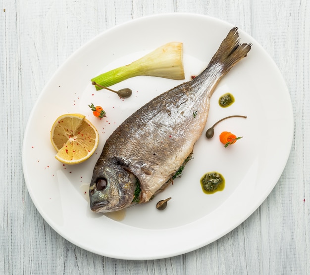 Pescado a la parrilla en un plato aislado en blanco. Vista superior de dorado asado entero