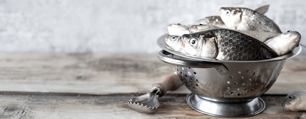 Foto pescado de río fresco crudo en un recipiente sobre una mesa de madera.