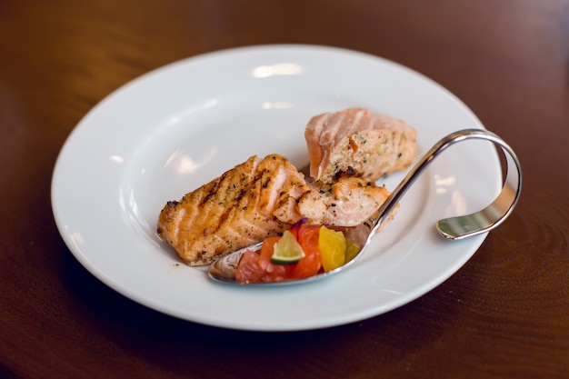 Pescado rojo en rodajas sobre una placa blanca en la que hay un tenedor de acero curvo y una cuchara en la mesa de madera marrón